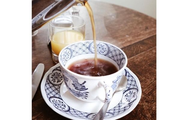 A silver coffee jug pours coffee into a blue and white Old Chelsea mug and saucer set.