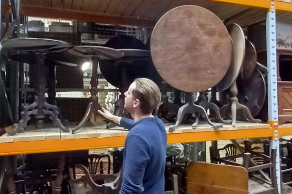 A person standing next to large shelves filled with wooden tables and chairs