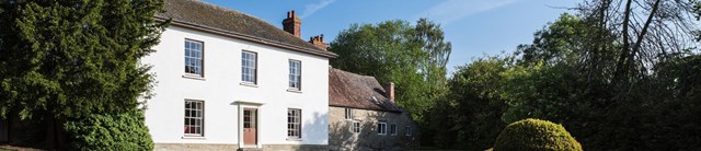 A white painted house surrounded by trees and hedges