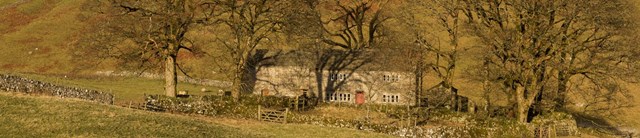 A small cottage surrounded by hills and trees with bare branches