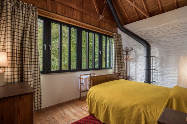 A bed with yellow sheets in front of a large window looking out onto greenery and trees