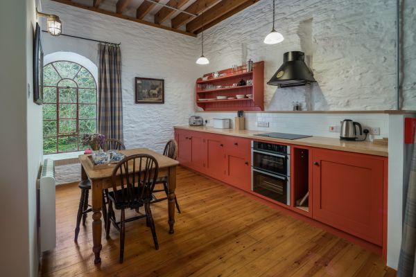 A kitchen with orange cupboards, a small wooden table and a large window